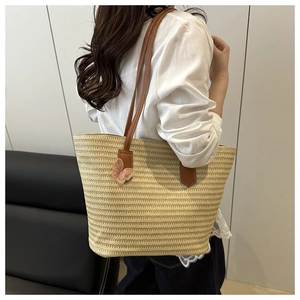 Close-up of woven straw tote bag with brown leather straps and pink mesh butterfly charm