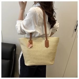 Detail of straw tote bag with brown leather strap and pink lace bow on model