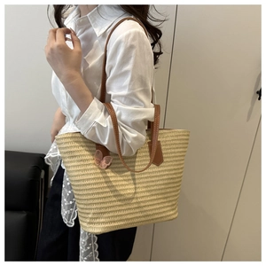 Detail of large straw woven tote bag with brown leather straps and pink butterfly charm