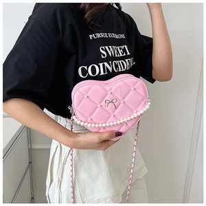 Detailed view of pink quilted heart-shaped crossbody bag with pearl chain and bow decoration