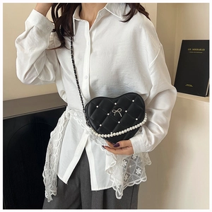 Close-up of heart-shaped quilted crossbody bag featuring pearls and a metal bow
