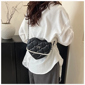 Macro detail of black heart-shaped quilted leather bag with pearl chain and silver bow
