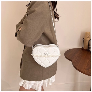 Detail of white heart-shaped quilted crossbody bag with pearl chain and bow decoration