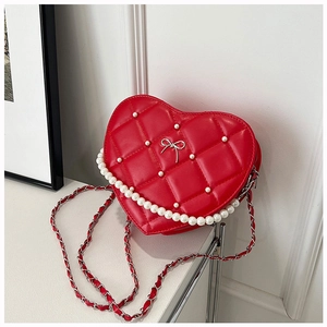 Macro detail of red heart-shaped quilted bag with pearl accents and silver bow