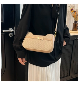 Detail of beige woven crossbody bag featuring a chic bow and gold metal hardware
