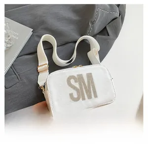 Close-up of white crossbody bag with large rhinestone SM letters and wide strap