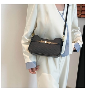 Detail view of the black textured shoulder bag featuring a gold bow and metallic accent