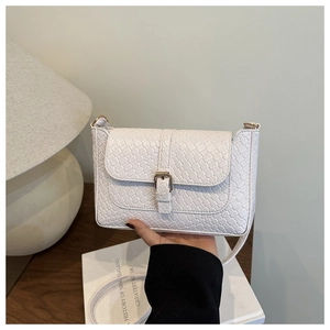 Detail view of white woven leather crossbody bag with gold buckle on a textured background