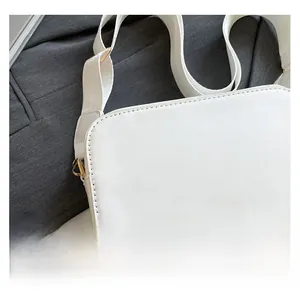 Detail of white leather crossbody bag with woven wide strap and golden metal buckle