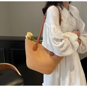 Détail d'un sac cabas en paille tissée avec anses en cuir marron foncé sur un mannequin