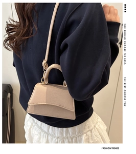 Side view of a beige trapezoid crossbody bag featuring lychee texture and slim strap
