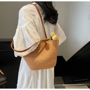 Détail d'un sac cabas tissé avec anses en cuir marron porté par un mannequin chic