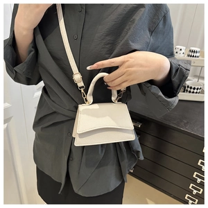 Detail of white lychee pattern mini crossbody bag with gold hardware on a gray shirt