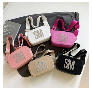 Detail of five colorful suede-style camera bags with rhinestone initials and wide straps