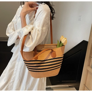 Sac cabas en paille à rayures noires et anses en cuir porté par un mannequin en robe blanche