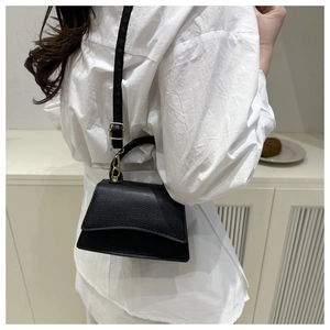 Detail of black lychee grain leather handbag with gold hardware and curved flap edge