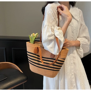Détail d'un sac cabas en paille tissée avec rayures noires et anses en cuir sur un mannequin