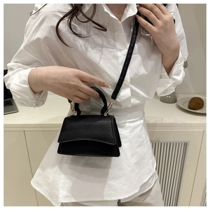 Close-up of black litchi pattern leather mini bag with gold buckle on a white outfit