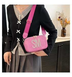 Pink suede crossbody bag featuring bold rhinestone SM letters and a wide shoulder strap