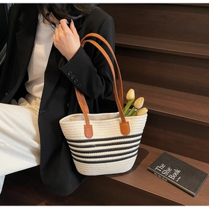 Détail du sac cabas tissé avec rayures noires et anses en cuir marron sur des escaliers