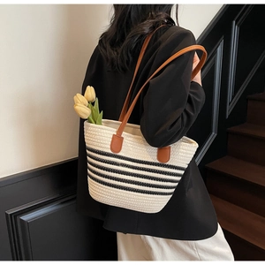 Détail d'un sac cabas tissé avec rayures noires et bandoulières en cuir marron