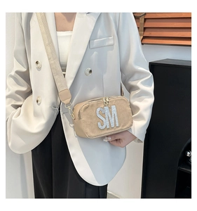 Detail of beige crossbody camera bag with rhinestone SM initials and wide fabric strap