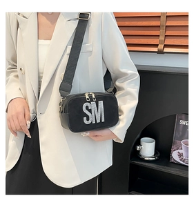 Close-up of black suede crossbody bag with rhinestone SM logo and wide nylon strap