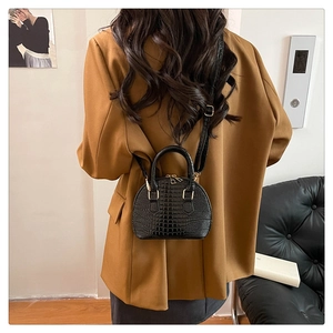 Dettaglio borsa a conchiglia nera con trama a coccodrillo su un blazer marrone