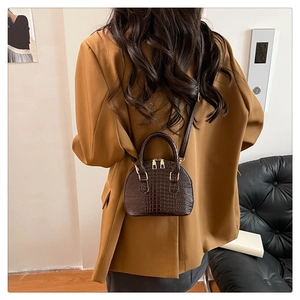 Modello che indossa una mini borsa a tracolla marrone scuro motivo coccodrillo su blazer