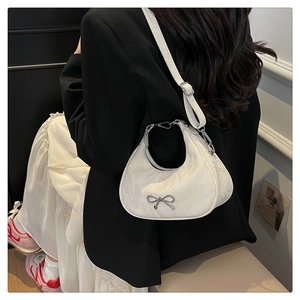 Detail of off-white pleated crescent bag featuring a silver bow buckle on model