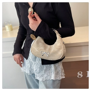 Close-up of beige crescent shoulder bag with silver bow ornament on a model