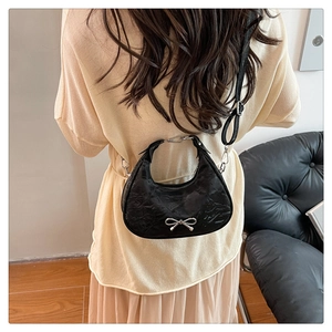 Close-up of black crescent bag with pleated texture and silver bow worn by a model