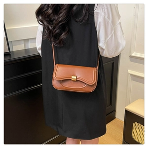Brown leather crossbody bag with wave design flap and gold clasp on a model