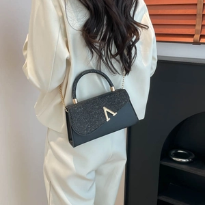 Chic black handbag with sparkling sequins and gold V buckle on elegant cream suit