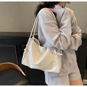 Detail of white glossy leather shoulder bag featuring textured folds and side knot detail