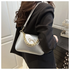 Detail of silver metallic shoulder bag with gold bow ornament and chain on black blazer