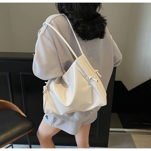 On-shoulder view of large white glossy drawstring tote bag with slim straps in a clean setting