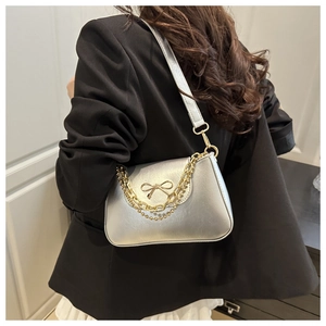 Detail of silver patent leather shoulder bag with golden bow and chunky chain strap