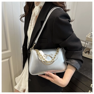 Detail of silver shoulder bag featuring a metallic bow buckle and golden double chains