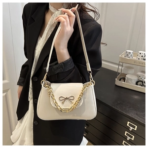 Close-up of beige PU leather shoulder bag featuring a metal bow and golden chain strap