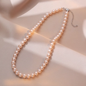 Elegant peach pearl necklace with silver lobster clasp on champagne satin background