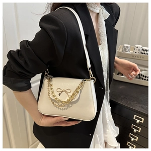 Close-up of beige underarm bag with gold bow ornament and chain strap on model