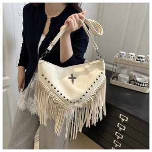 Detail of hobo bag with metallic studs, a gothic cross charm, and long tassels decoration