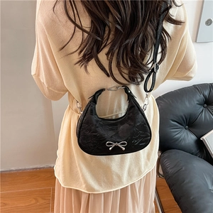 Chic black pleated crescent bag with silver metallic bow on interior model background