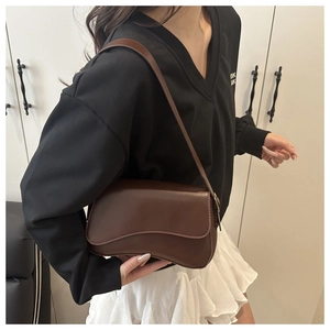 Detail of dark brown leather underarm bag with unique wavy edge flap and chic magnetic buckle