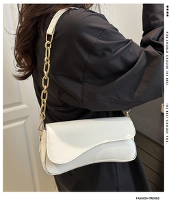 Close-up of white glossy leather handbag with curved flap and gold chain strap detail