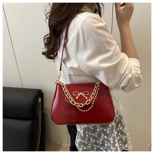 Close-up of red leather underarm bag featuring a gold bow logo and metal chain detail