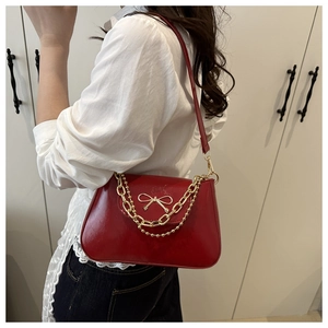 Detail of red patent leather shoulder bag featuring a gold bow buckle and chain strap