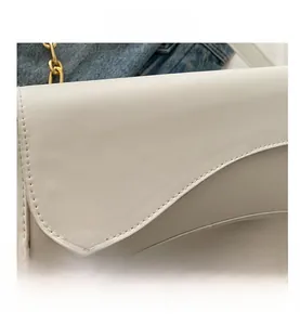 Detail view of white leather saddle bag showing precise stitching and metallic chain