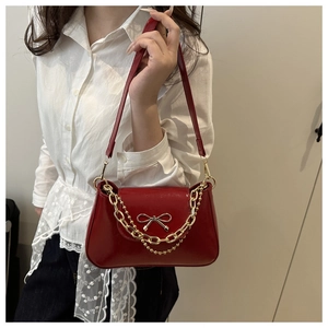 Close-up of red patent leather shoulder bag with golden bow and chain decoration